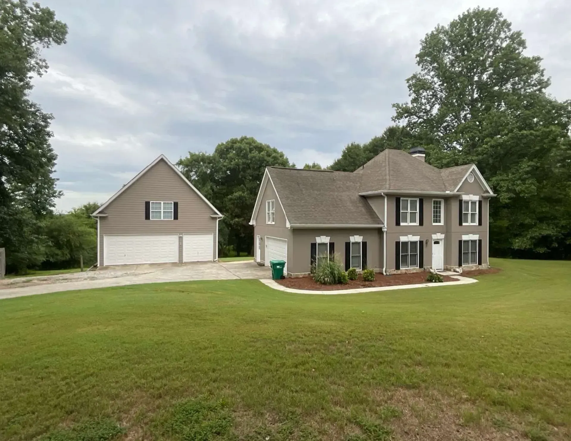 Large beige two-story house with detached garage on a grassy lawn under cloudy skies