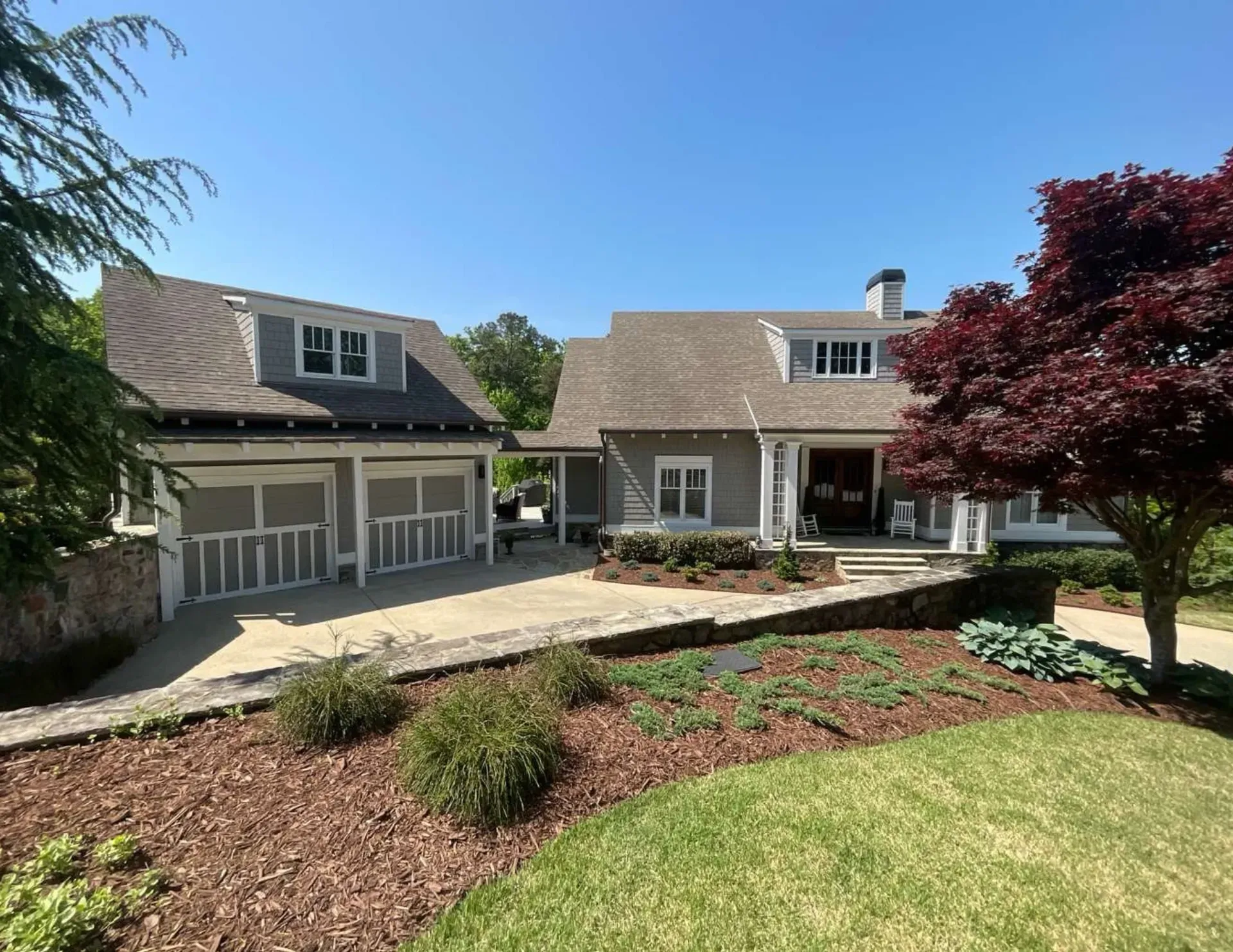 Suburban house with attached garage, landscaped front yard, and large tree under a clear blue sky