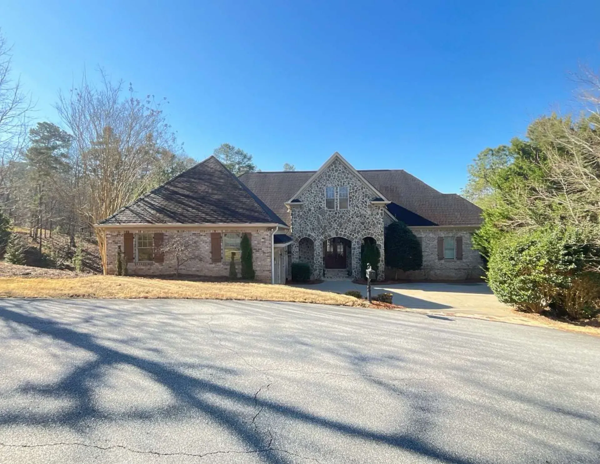 Stone house with a two-car garage, arched front entry, and a sunny driveway under a clear blue sky
