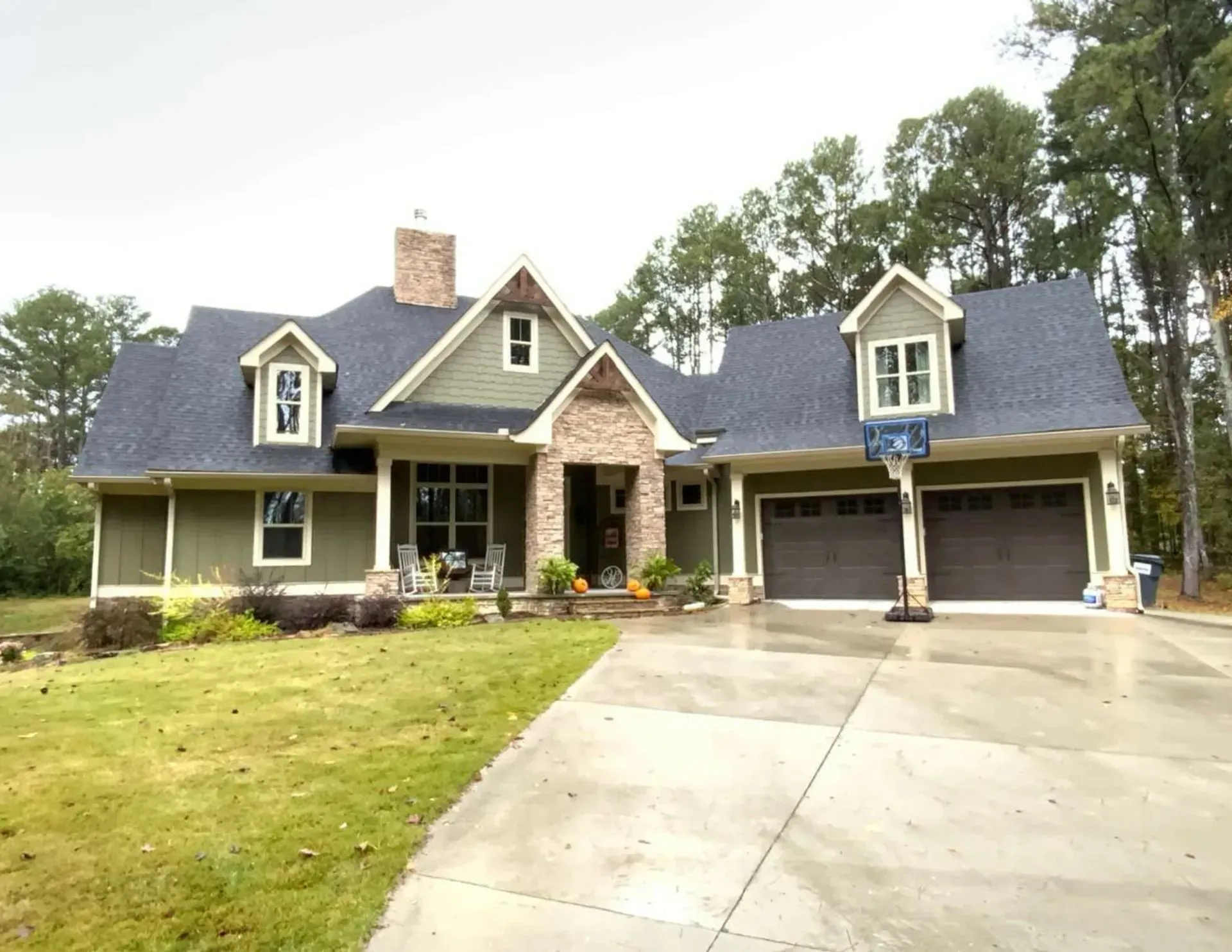 Large gray suburban house with stone accents, front porch, and a two-car garage beside a concrete driveway.