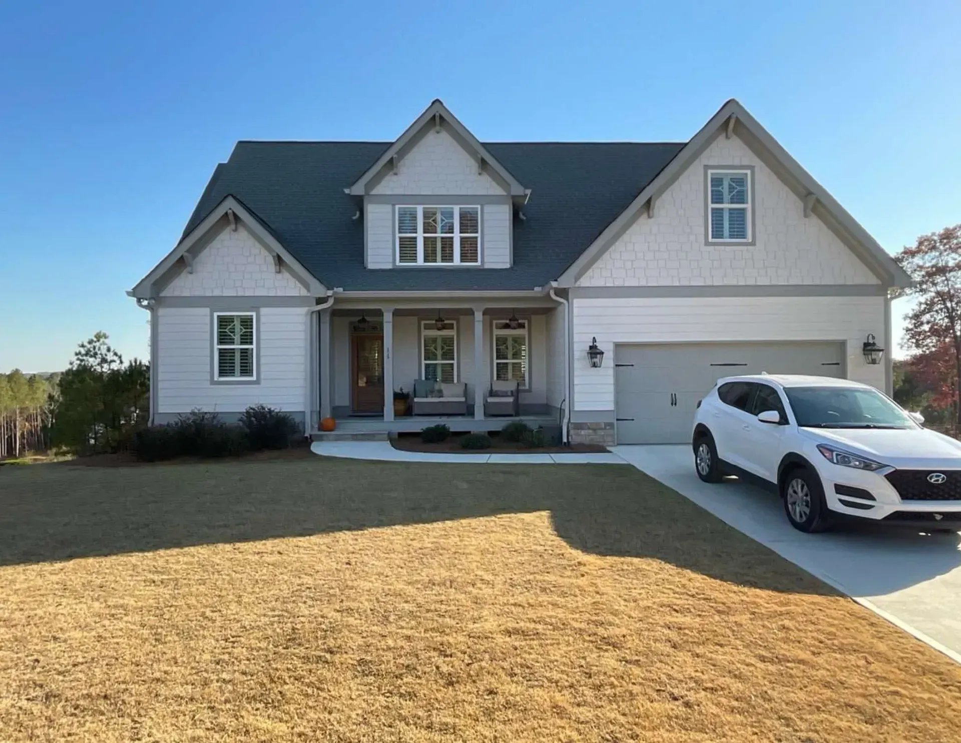 Suburban house with gray siding, front porch, and white SUV parked in the driveway.