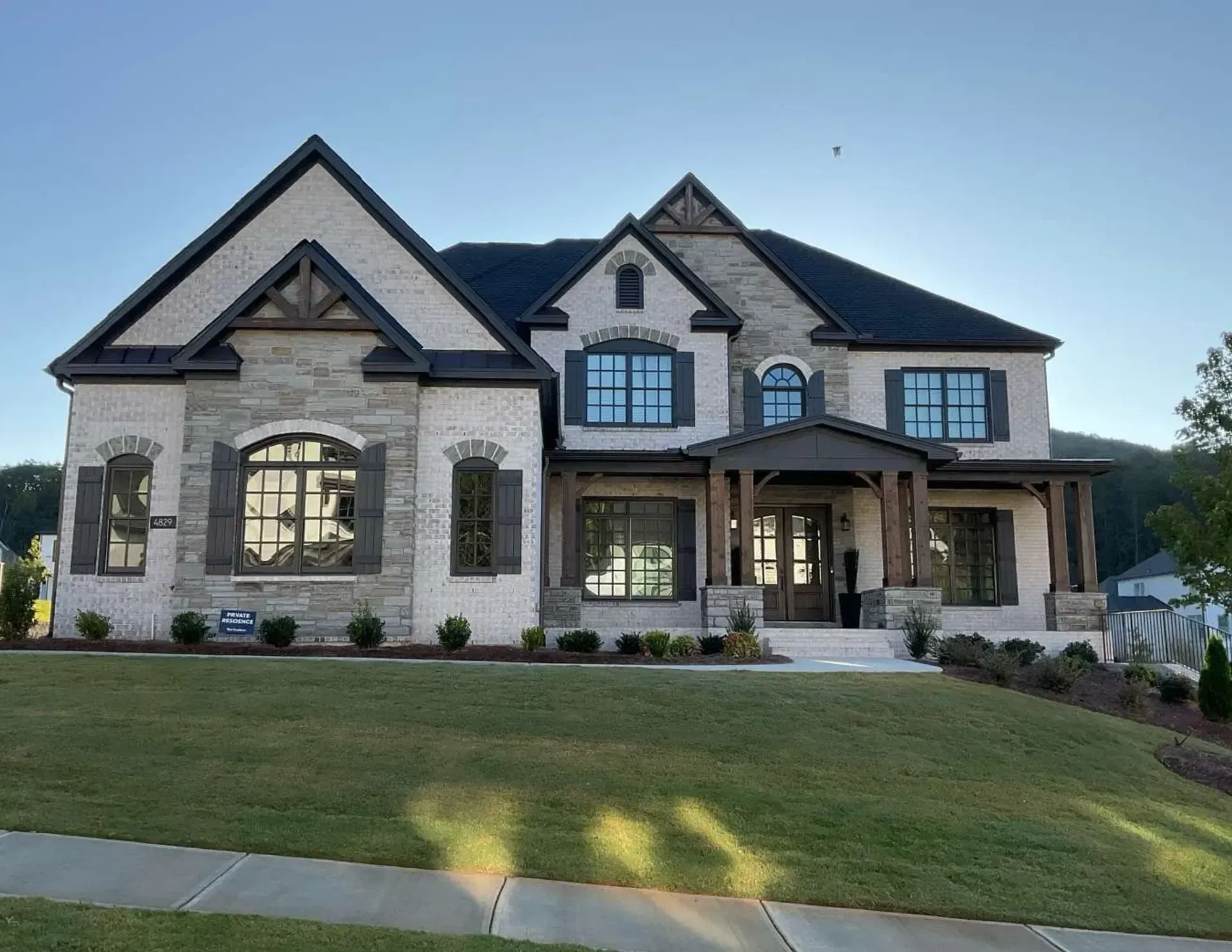 Large two-story stone and siding suburban house with manicured lawn at dusk