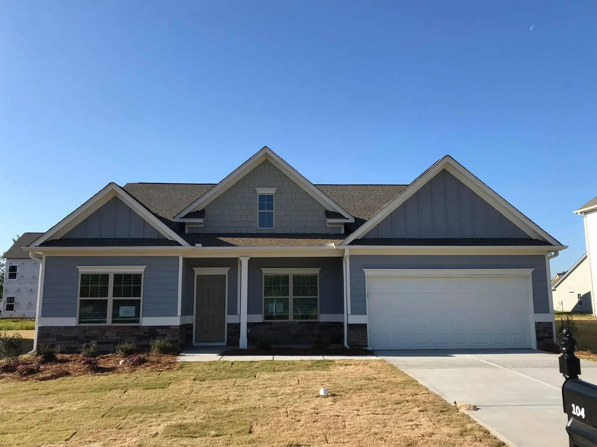 Single-story gray house with a front porch, gabled roof, and two-car garage under a clear blue sky