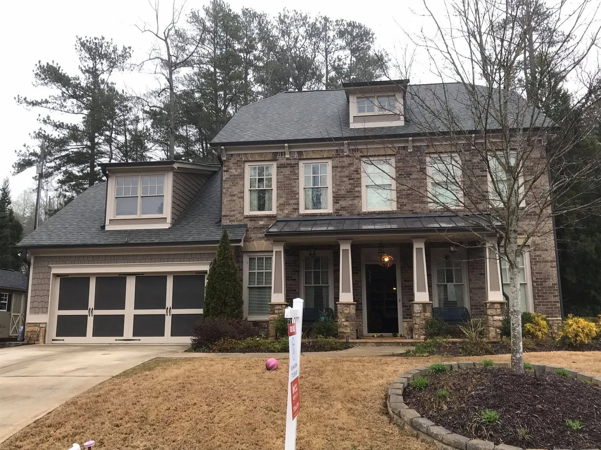 Large brick suburban house with attached garage, front porch, and winter landscaping