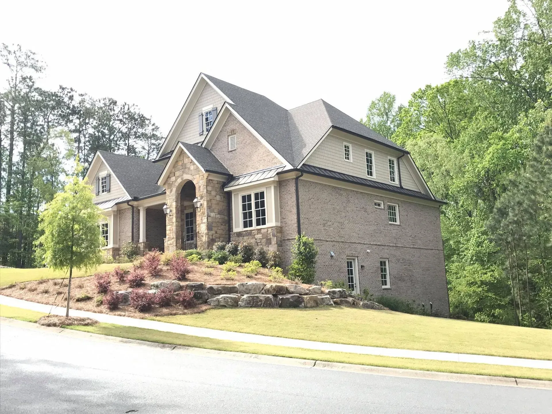 Stone house with gabled roof and covered porch on a landscaped corner lot beside a curved road