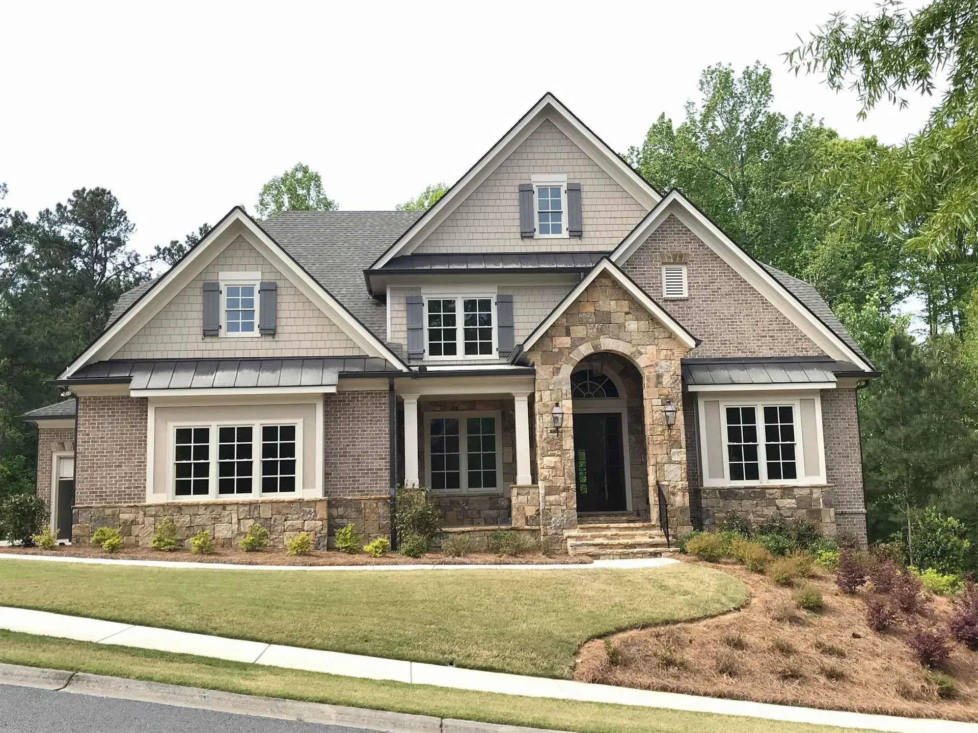 Large beige suburban house with stone accents, gabled roof, and landscaped front yard