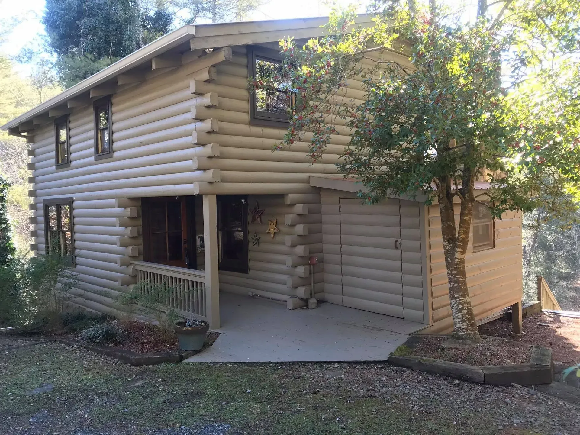 Log cabin-style house with a covered porch and garage, surrounded by trees and landscaping
