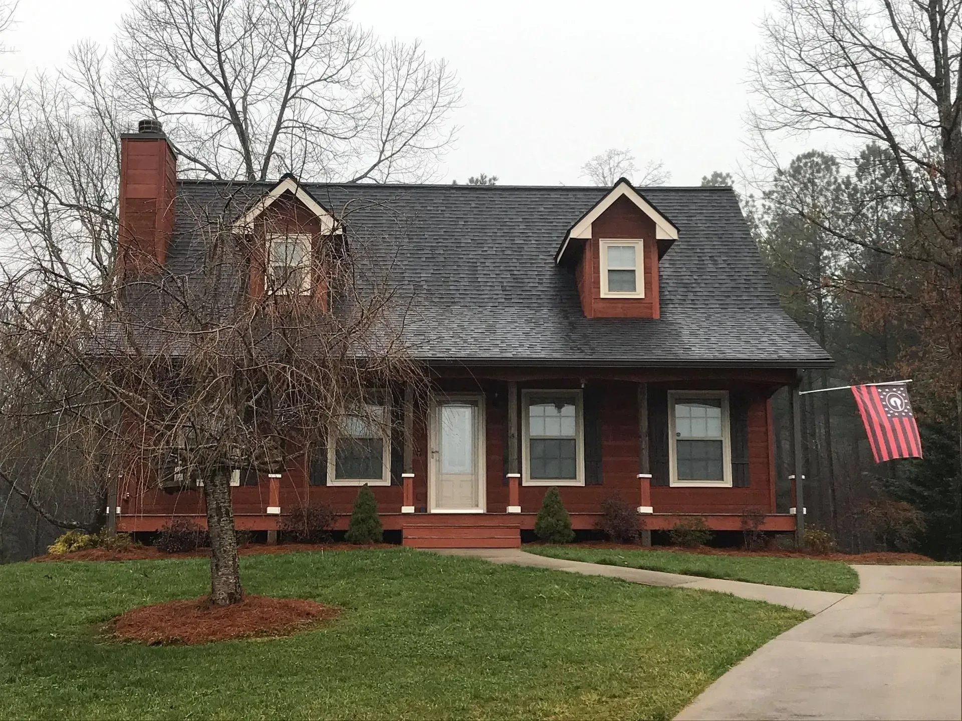 Brick house with dark roof, red trim, and American flag, fronted by a lawn and driveway
