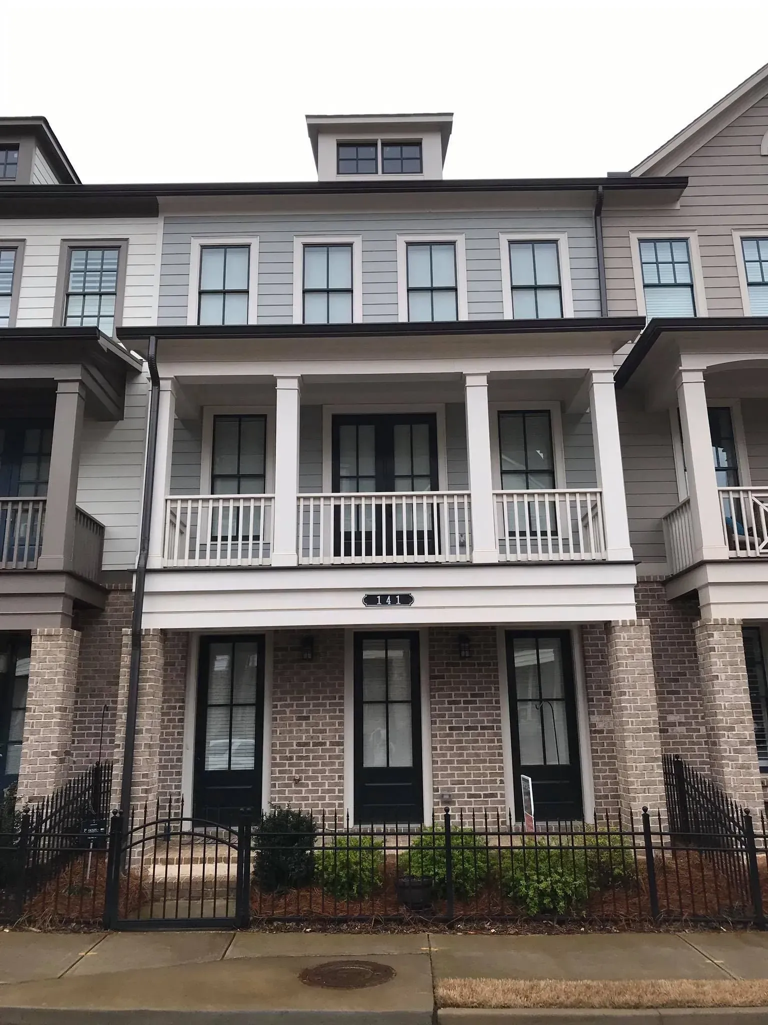 Row of townhouses with gray siding, white trim, and front porches along a sidewalk