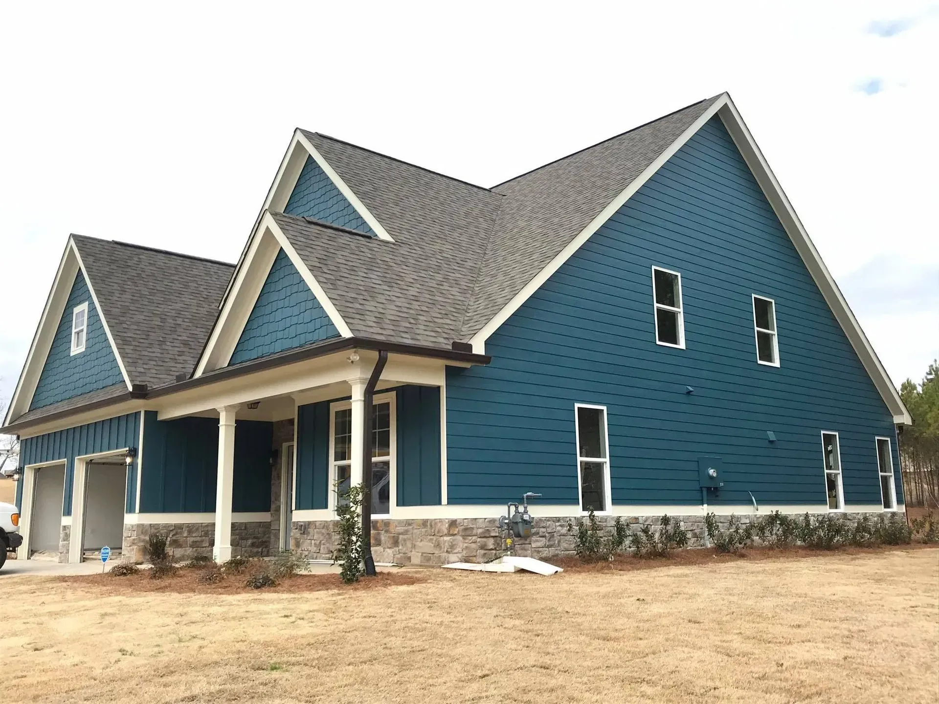 Blue house under construction with steep gabled roof and white trim on a bare lot