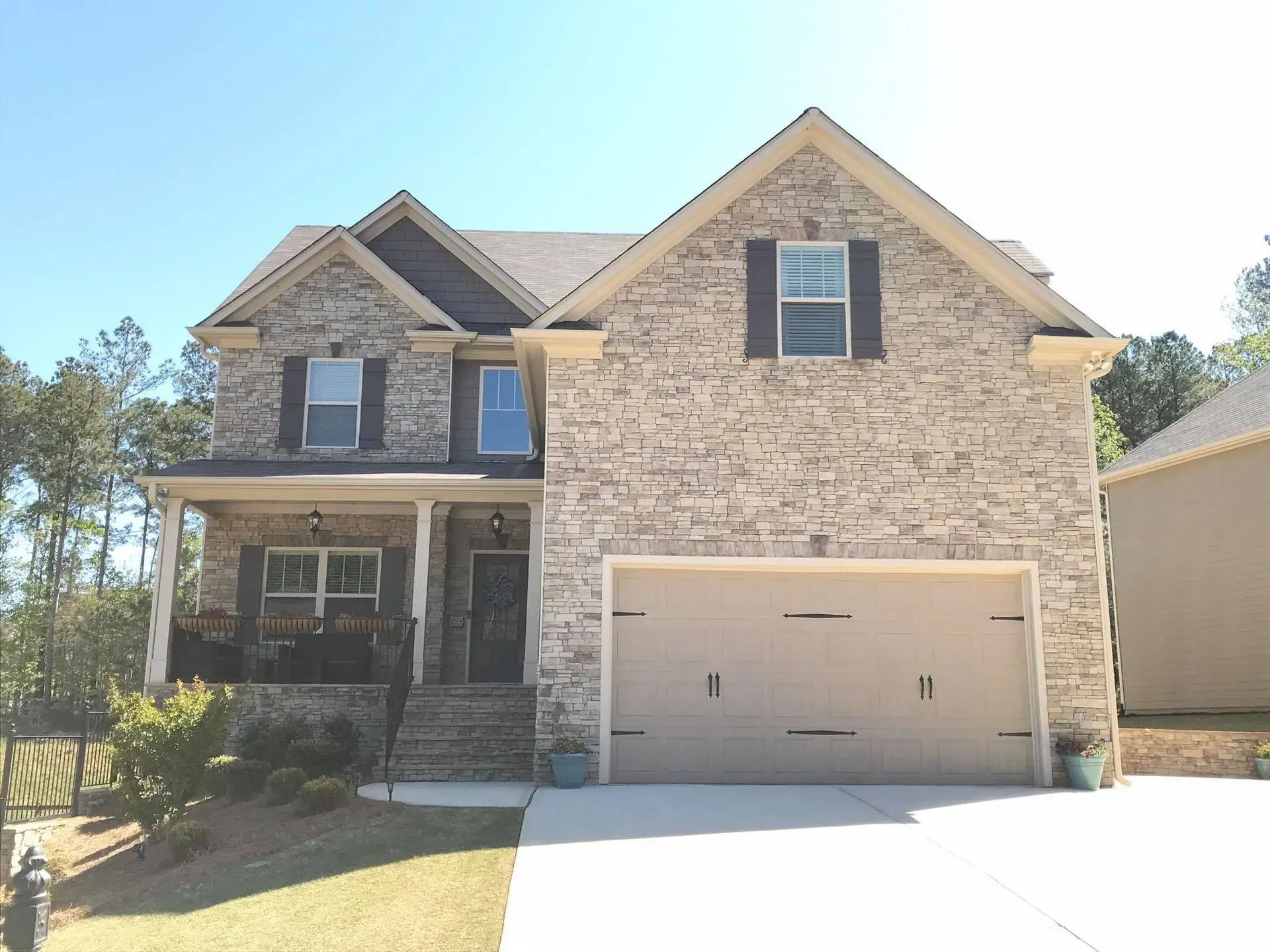 Two-story beige brick house with a front porch and double garage under a clear blue sky