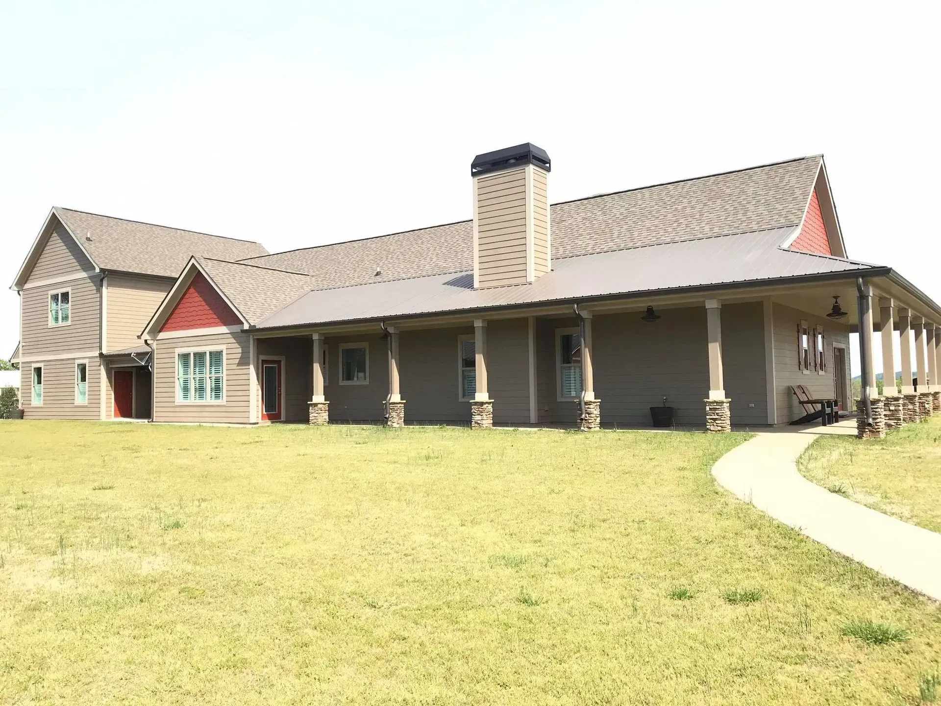 Modern house with a covered porch, tan roof, and curved walkway on a grassy lawn