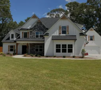 Large white house with gabled roof, stone accents, and a wide green lawn under a blue sky