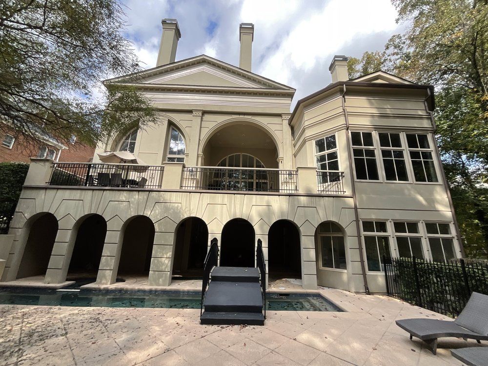 Historic cream-colored mansion with arched porch, balcony, and large bay windows under a partly cloudy sky