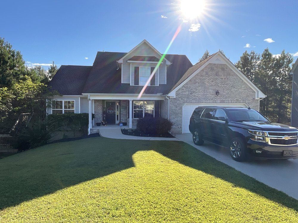 Suburban brick house with a dark SUV parked in the driveway under bright sunlight.