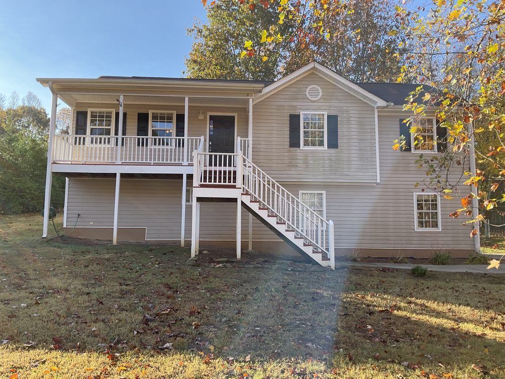 Gray house with front porch, staircase, and white railings on a grassy hillside in autumn.