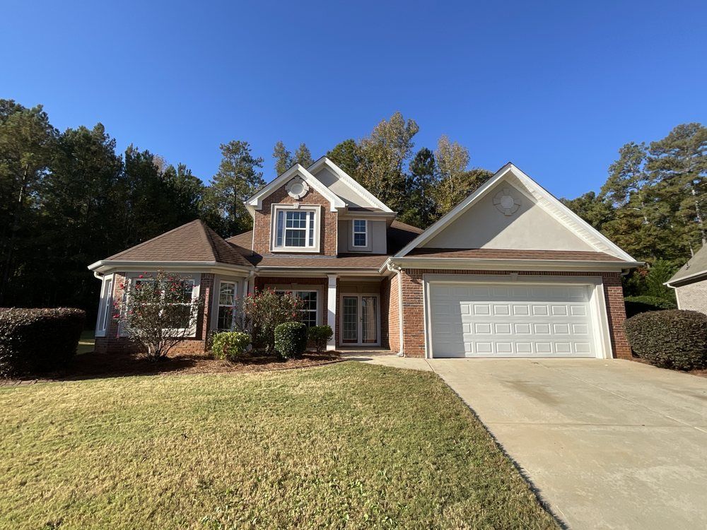 Two-story brick house with white garage, front porch, and sloped driveway on a sunny day