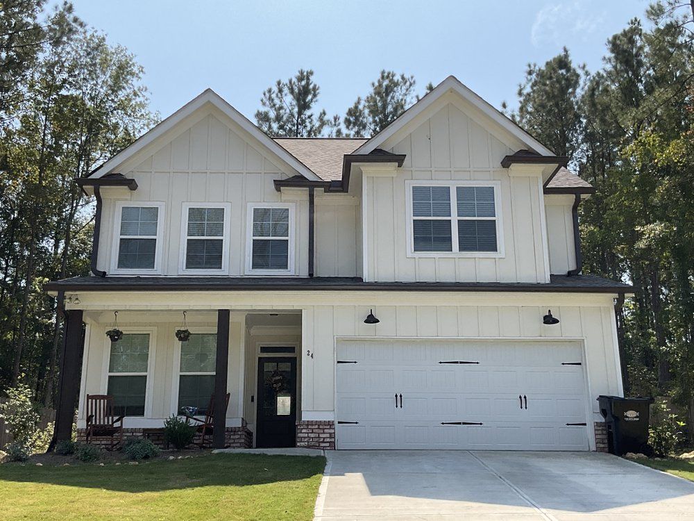 Two-story beige house with white trim, front porch, and double garage under a clear blue sky
