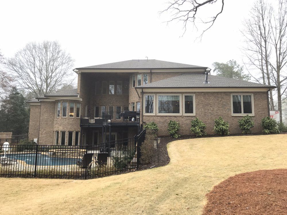 Large brick house with a covered patio, fenced pool, and sloped grassy yard in winter.