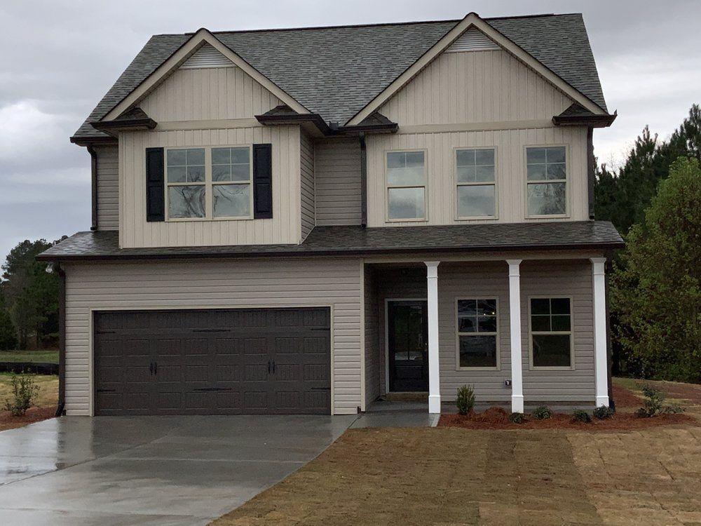 Two-story gray suburban house with a dark garage door and wet driveway