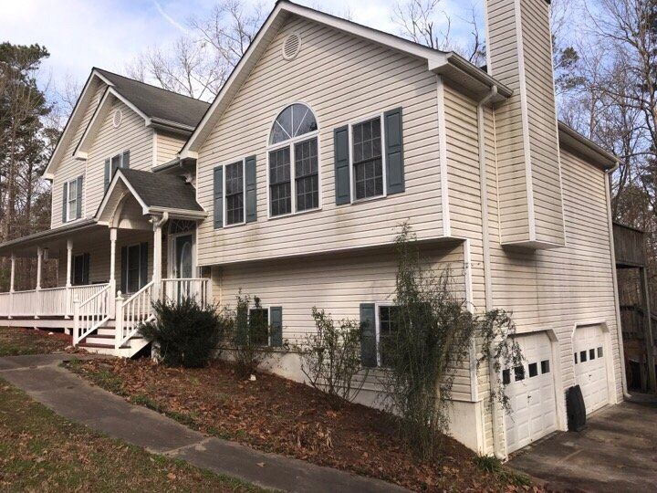 Two-story beige house with porch, large arched windows, and a garage on a sloped lot