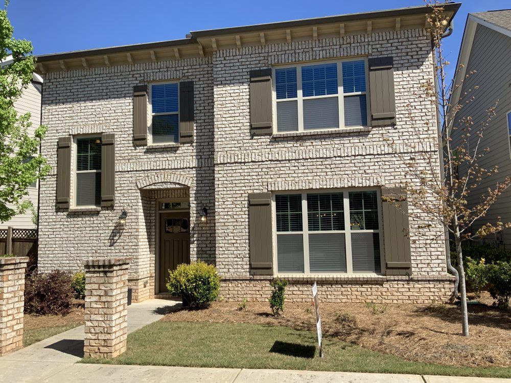 Two-story brick townhouse with white trim, front lawn, and small porch under a clear blue sky