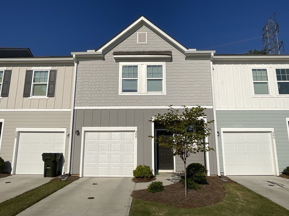 Row of beige townhouses with white garage doors and a small tree in front under a clear blue sky