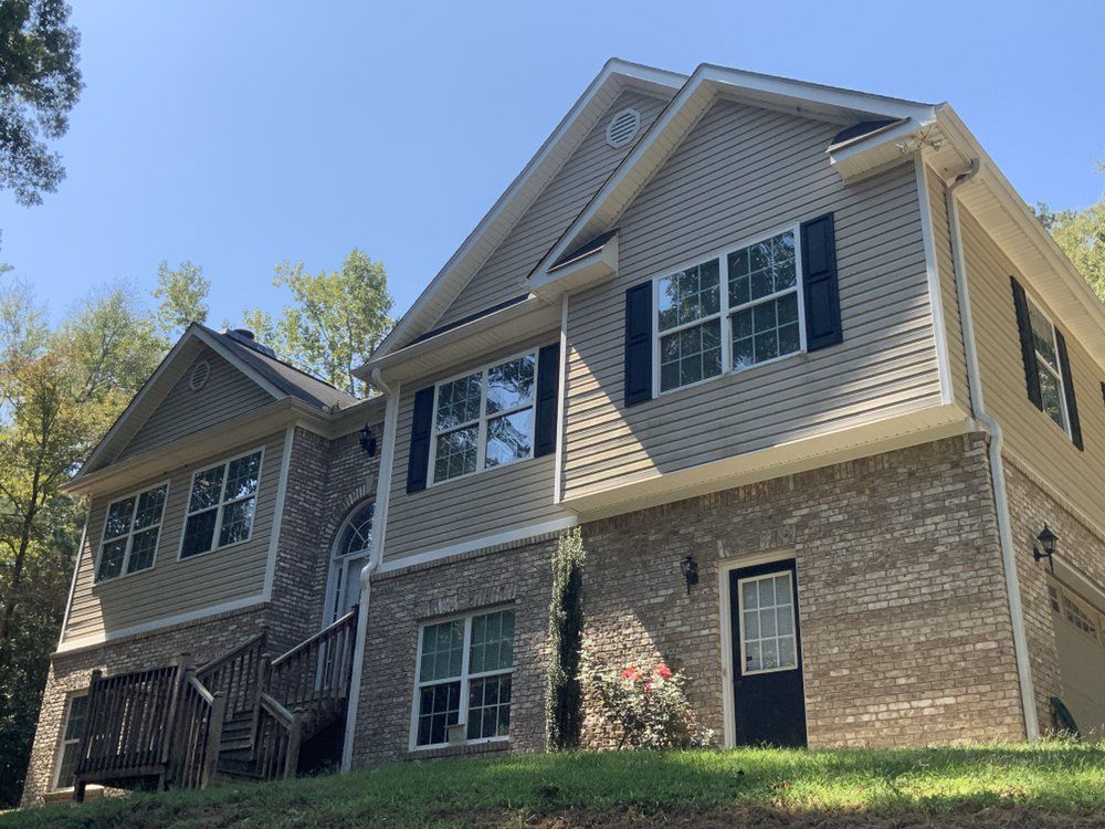 Two-story suburban house with beige siding, stone facade, and black shutters under a blue sky