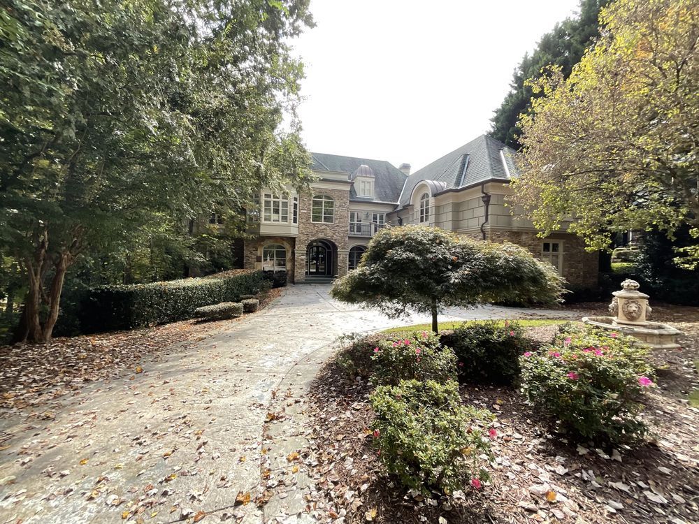 Mansion driveway lined with trees and hedges, leading to a stone building with arched entrance.
