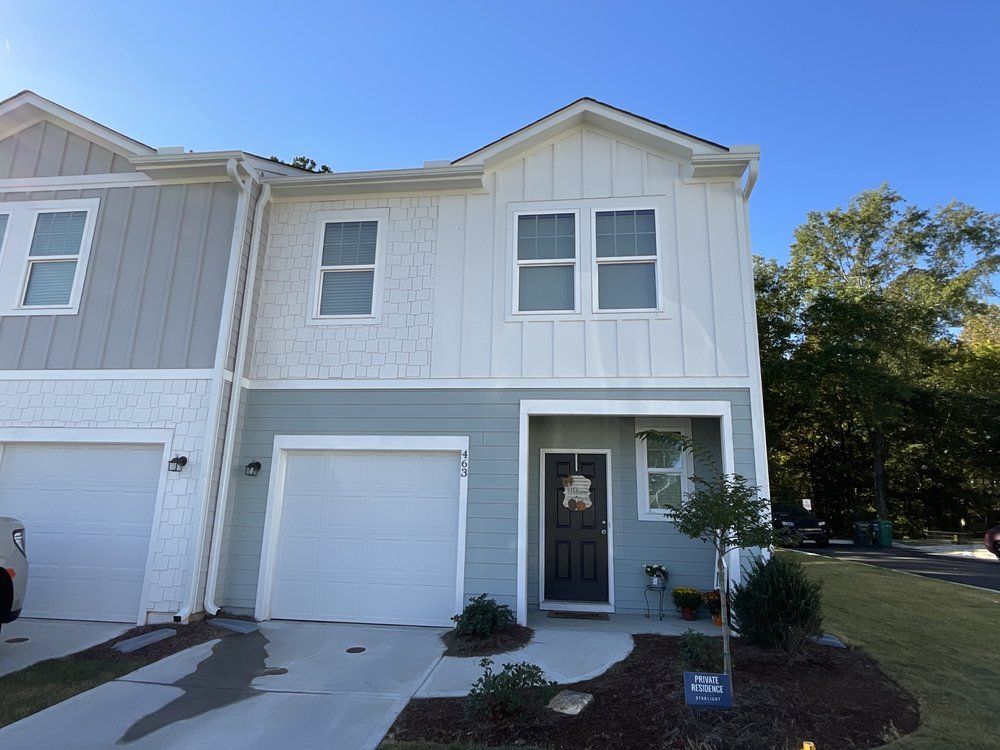 Two-story townhouse with gray siding, white trim, and a single-car garage under a clear blue sky