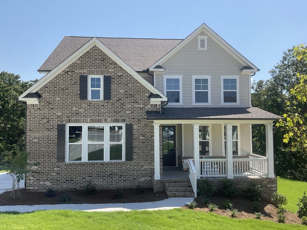Two-story gray house with stone facade and a covered front porch on a sunny day