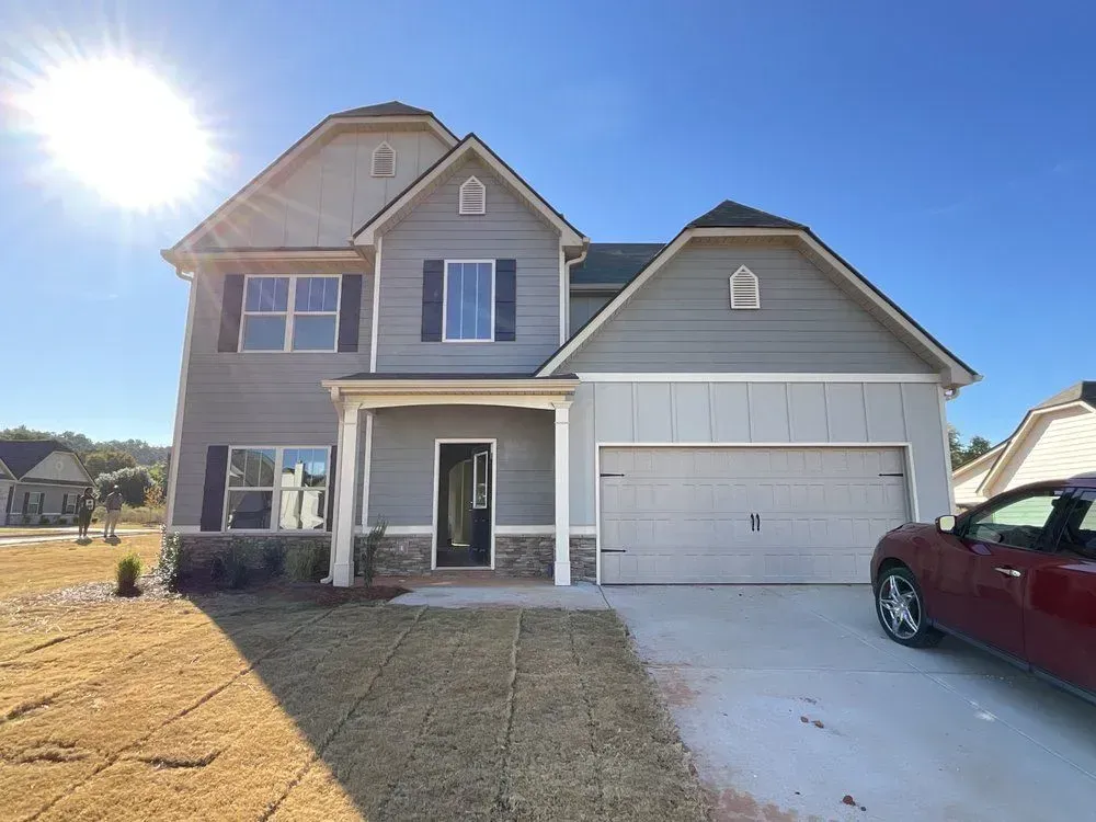 Two-story suburban house with beige siding, front porch, and a two-car garage in bright sunlight