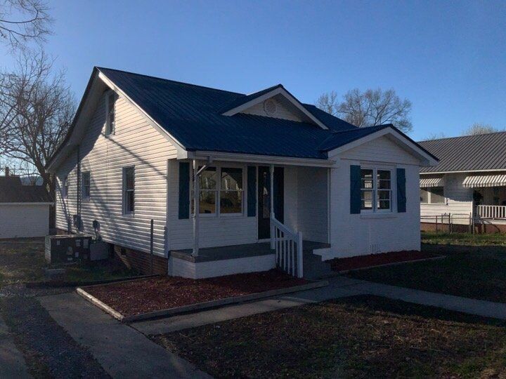 White house with blue roof and front porch, seen from the yard on a sunny day