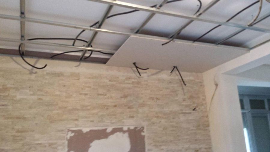 Soffitto in costruzione: struttura in metallo, cavi elettrici, cartongesso e muro in pietra parzialmente rifinito.