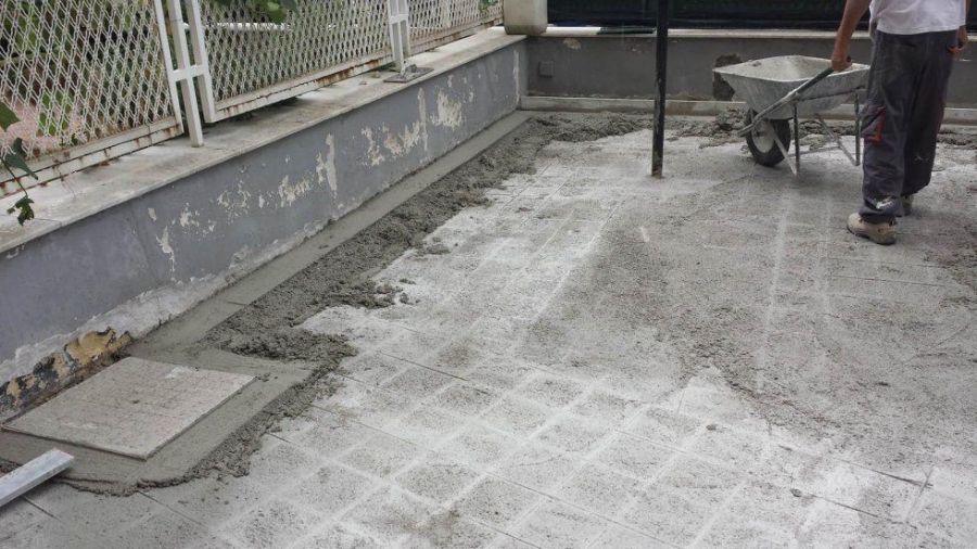Persona che usa una carriola per stendere il cemento su un patio piastrellato. Il cemento è appena stato steso.