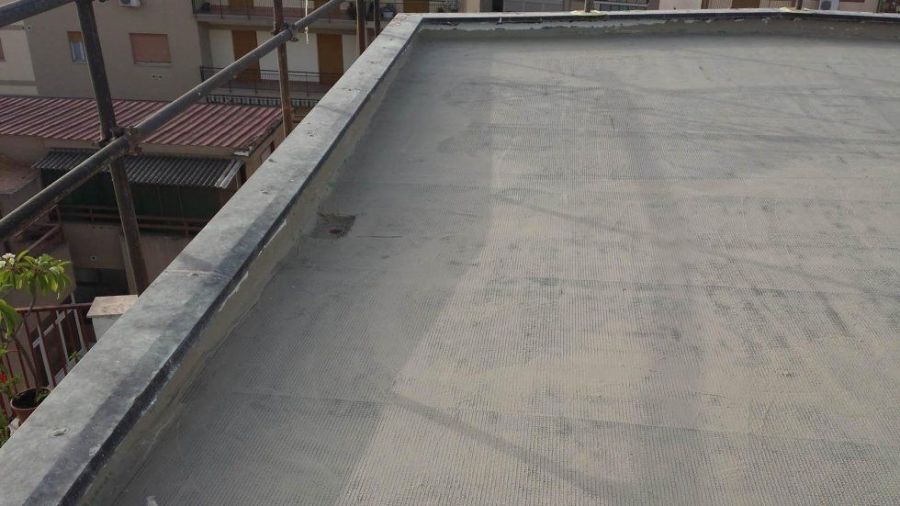 Vista di un tetto piatto e grigio con un bordo metallico e un'impalcatura sullo sfondo.