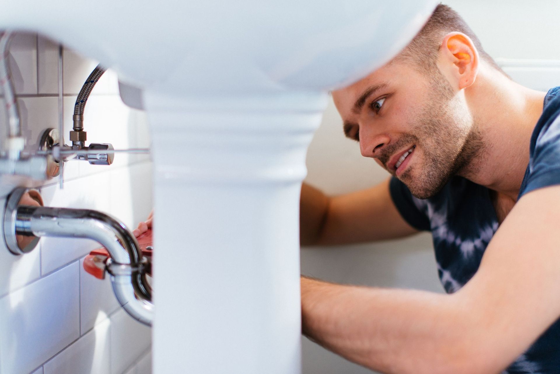 Person repairing plumbing under a sink with tools and exposed pipes