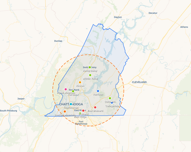Map with green and blue outlined regions, a red location pin, and a dashed orange radius circle.