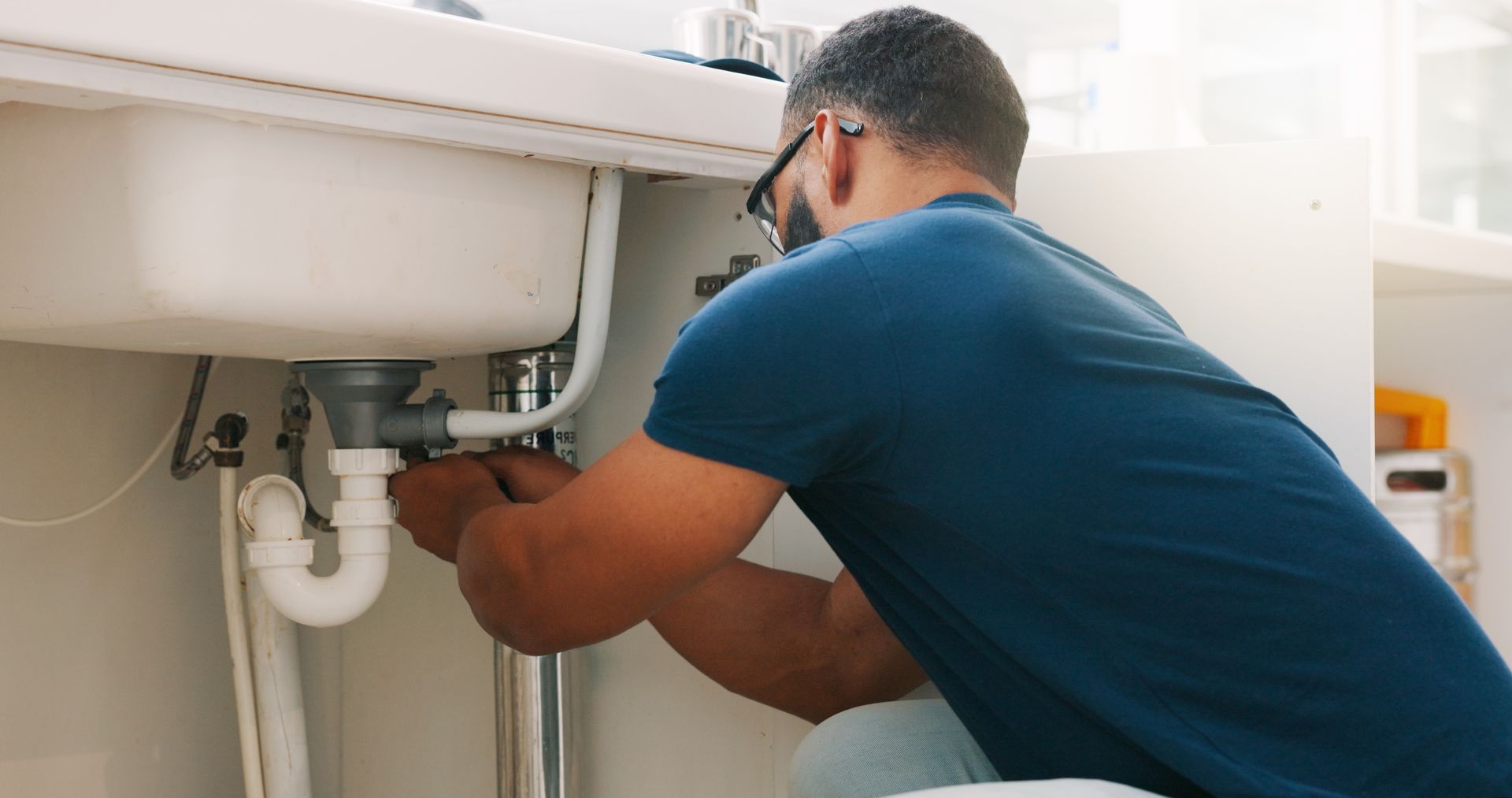 Plumber repairing pipes under a sink in a bright kitchen or bathroom
