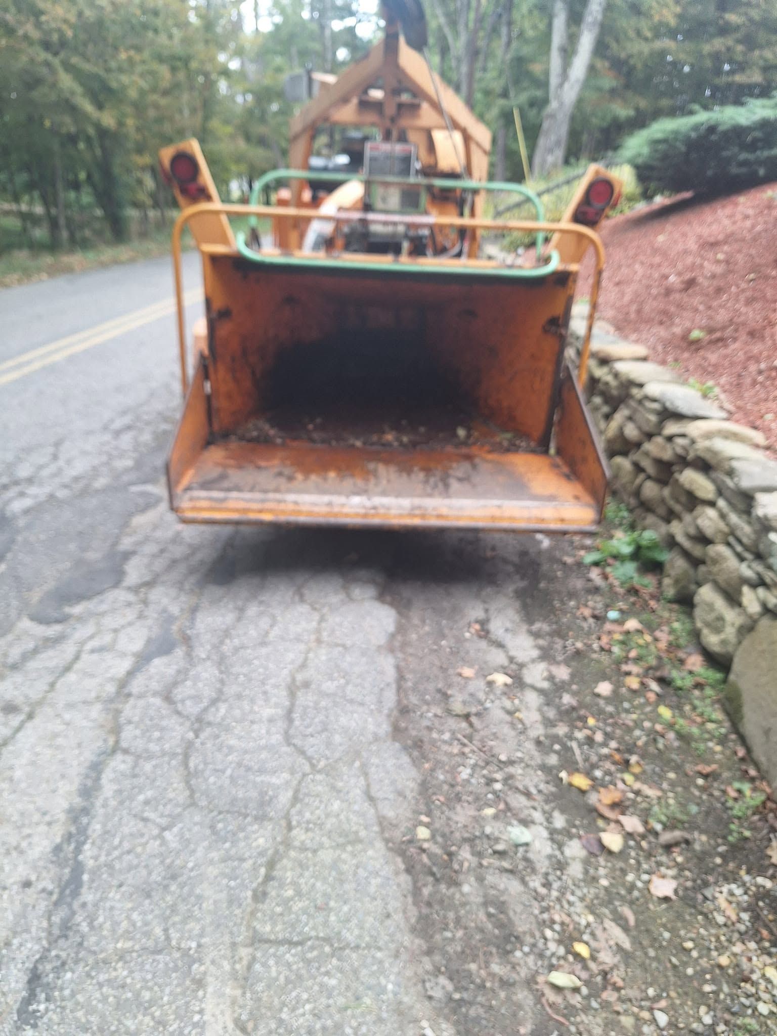 Orange construction loader bucket blocking a cracked road in a wooded area