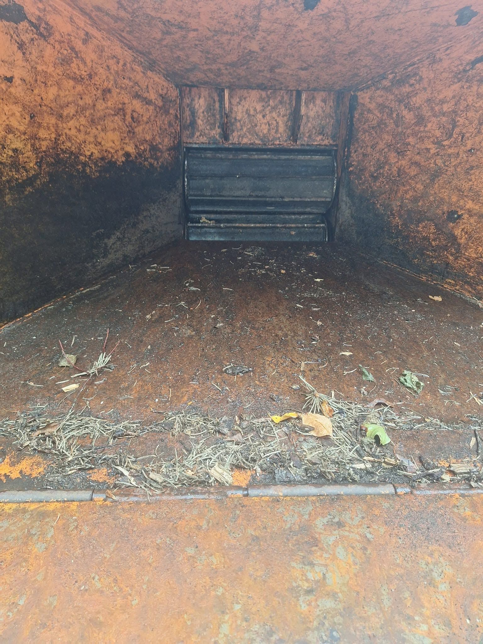 Rusty metal interior of an empty dumpster with scattered debris on the floor