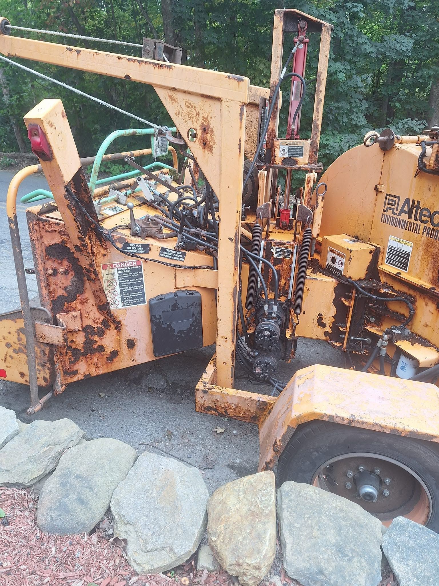 Rusty yellow construction machine beside rocks and greenery outdoors
