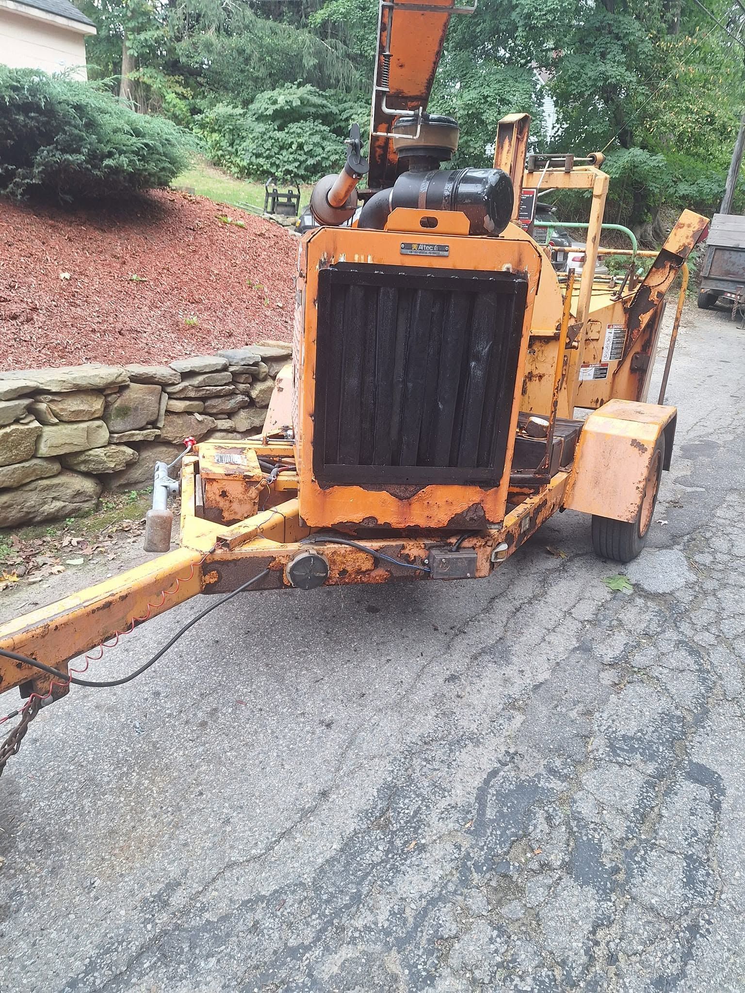 Orange construction vehicle on a narrow road beside a stone wall and wooded embankment
