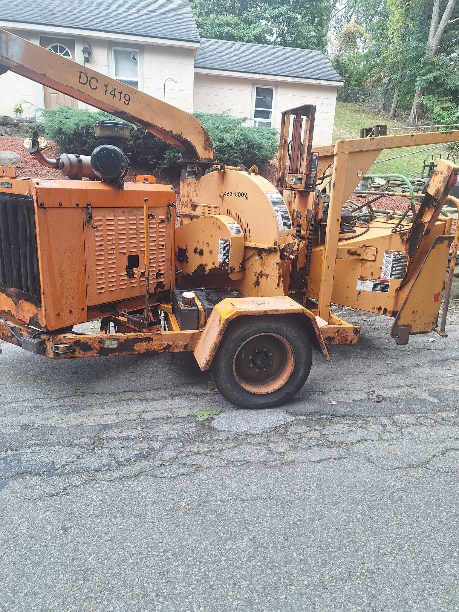 Orange wood chipper trailer parked on a gravel driveway in front of a house