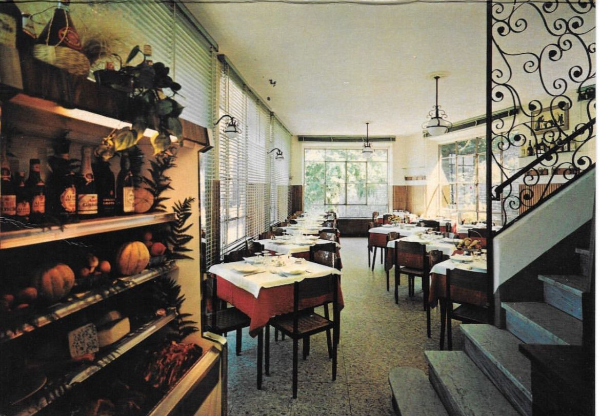 Interno di un ristorante con tavoli apparecchiati per mangiare, scaffali con prodotti esposti e una scala.