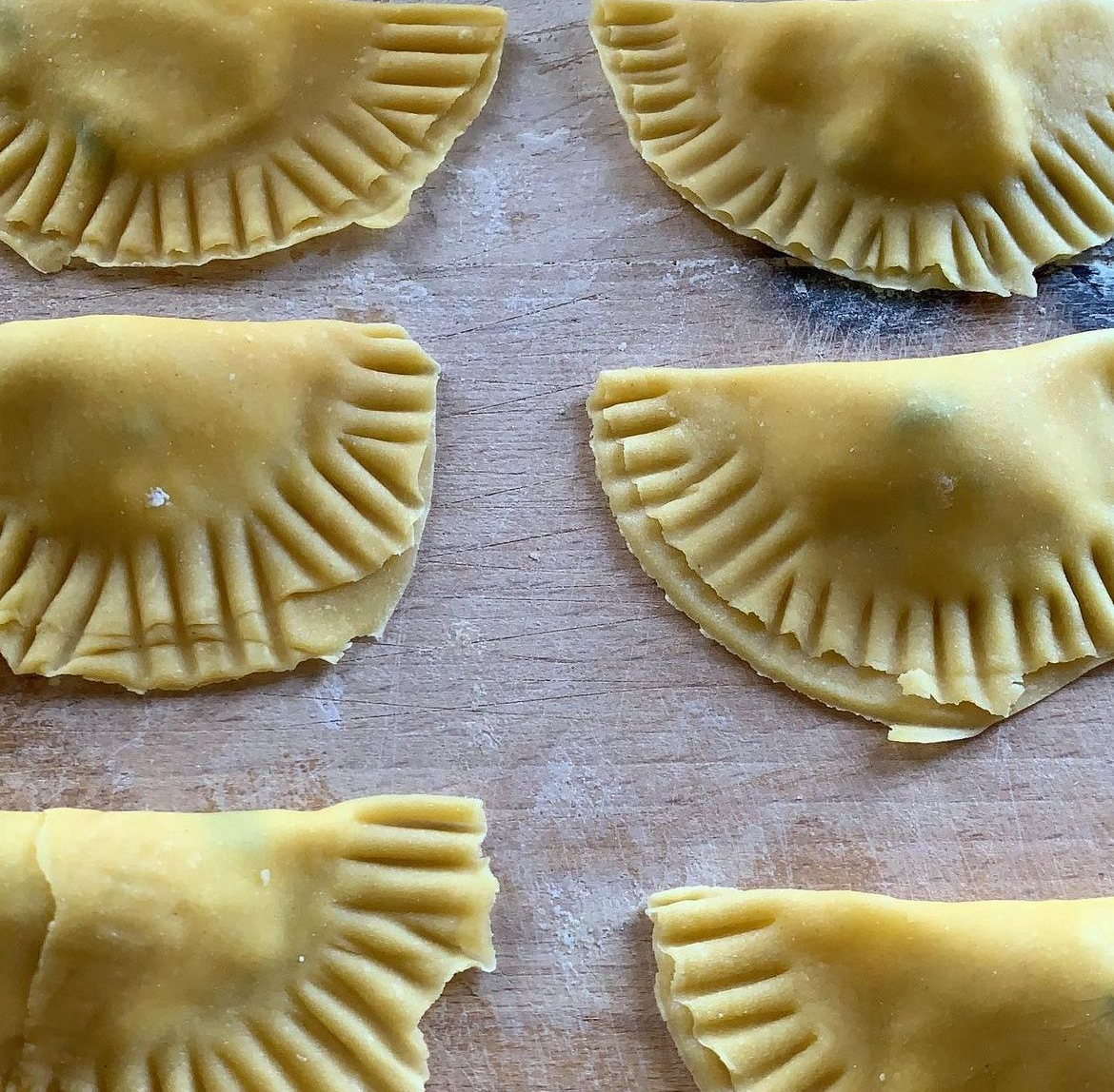 Primo piano di sei ravioli gialli con bordi arricciati su una superficie di legno.
