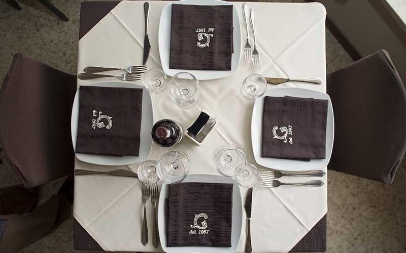 Tavolo apparecchiato per quattro, bianco e marrone, con tovaglioli e posate.