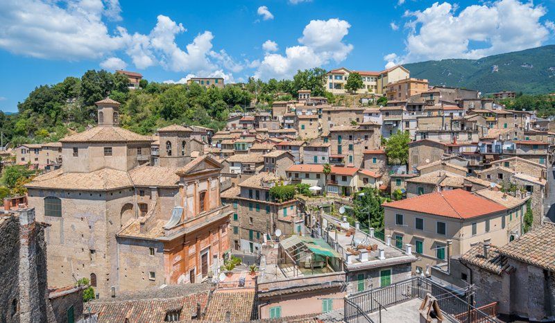 Paesaggio urbano di vecchi edifici con tetti in terracotta, sotto un cielo azzurro, adagiati sul pendio di una collina.