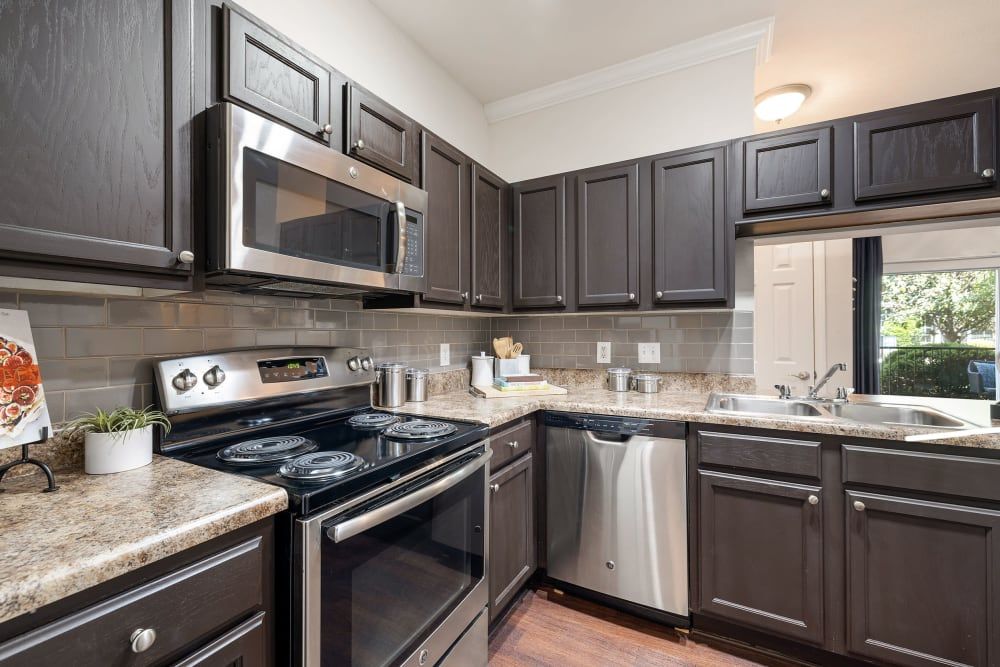 a kitchen with black cabinets, stainless steel appliances, a stove, a microwave, and a dishwasher at Marquis Carmel Valley in Charlotte, NC.