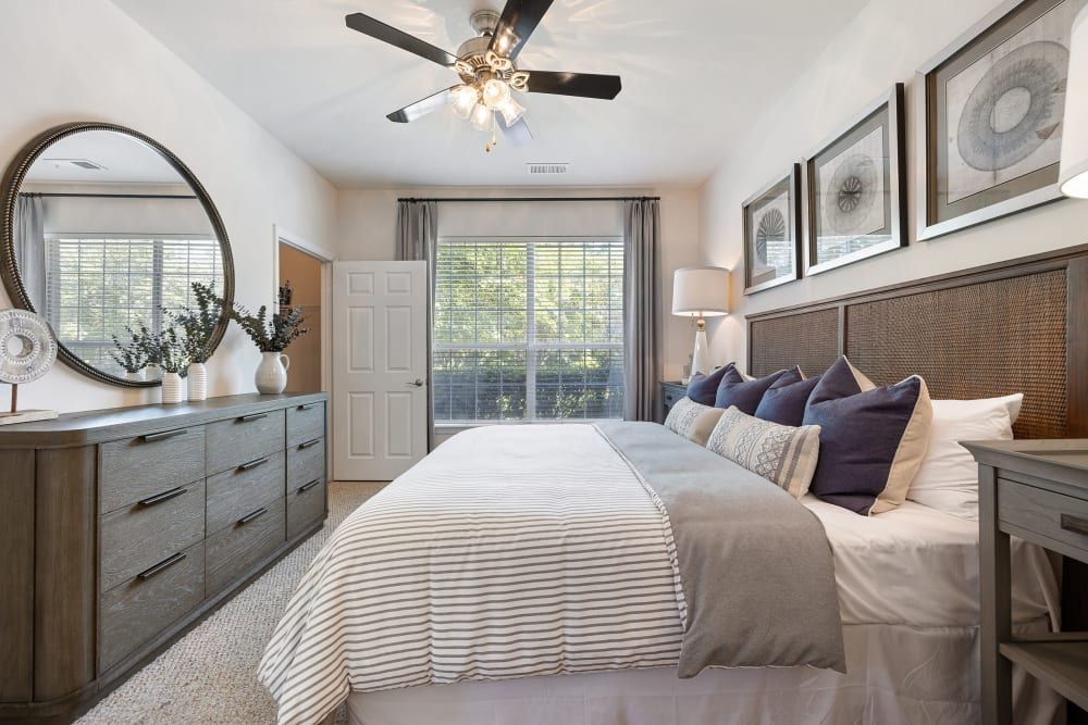 a bedroom with a large bed, dresser, mirror, and ceiling fan at Marquis Carmel Valley in Charlotte, NC.